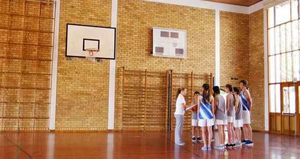 Female coach instructing school students in basketball court