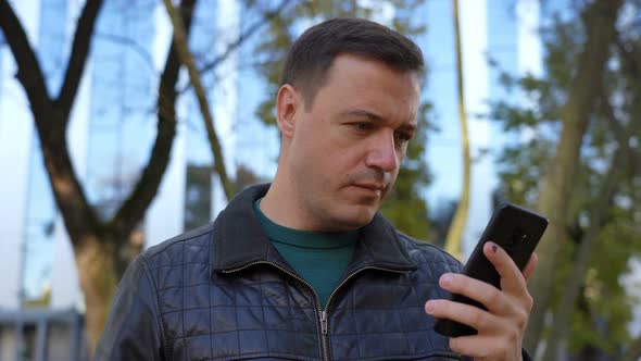 Excited Guy Looks at Phone and Celebrates Big Win Financial Good News Phone Near Modern Building