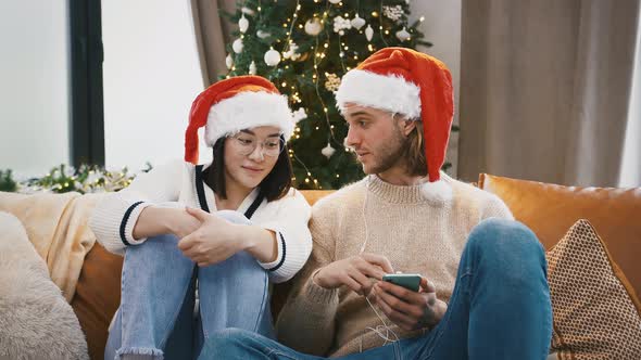 Mixed Race Friends Listening to Music Through Earphones on Smartphone Sitting on Sofa Against