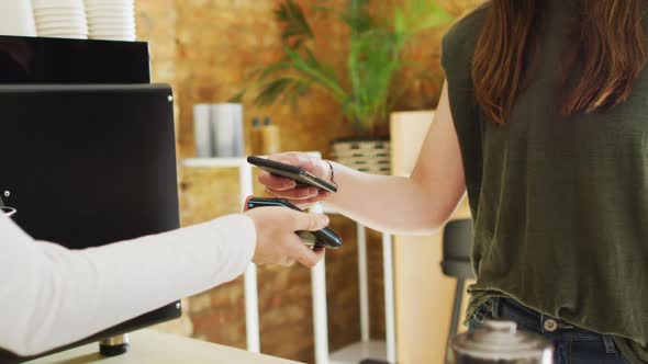 Caucasian waitress receiving contactless payment and giving coffee cup to caucasian female customer