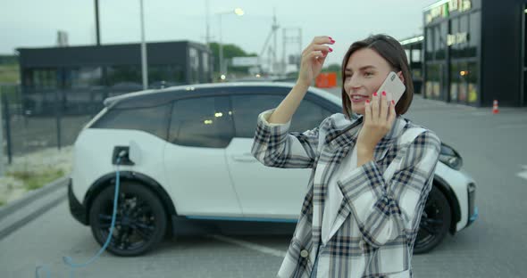Young Woman Talking on the Phone Near Electric Car