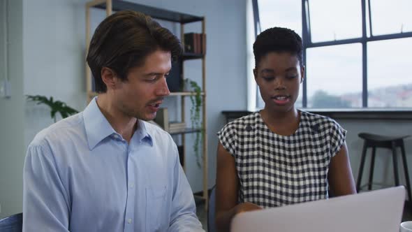 Diverse business colleagues sitting at desk using laptop going through paperwork in office