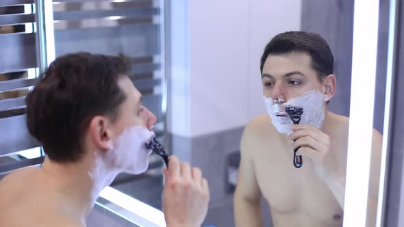 Handsome Man Shaving His Beard in Bathroom By Mechanical Razor