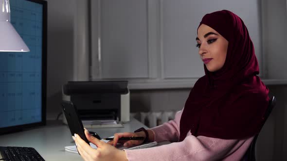 Muslim Business Lady in Hijab Speaks By Videocall on Her Smartphone and Makes Notes