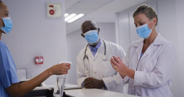 Diverse hospital worker disinfecting hands of doctors all wearing face masks