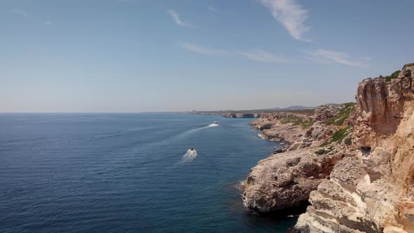 AERIAL: Drone flying beside cliffs of mallorca coastline with boats in summer