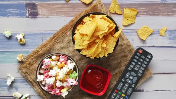 Top View of a Bowl of Popcorn Chips and Tv Remote on Wooden Background
