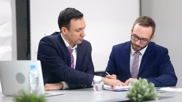 Focused Man Boss in Suit Collaboration with Male Employee Writing Notes at Workplace