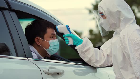 doctor in protective PPE suit using infrared thermometer measuring temperature of man