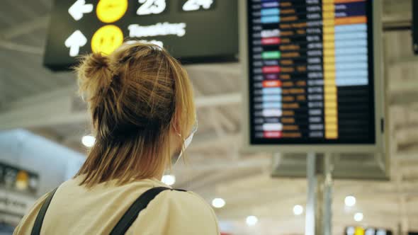 Woman Wearing Medical Mask Looking at Time Table Screen Departure Schedule at Airport