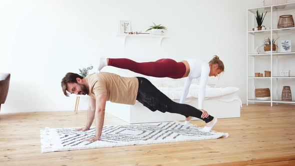 Loving Young Couple Having Acro Yoga Practice Near Bed at Home