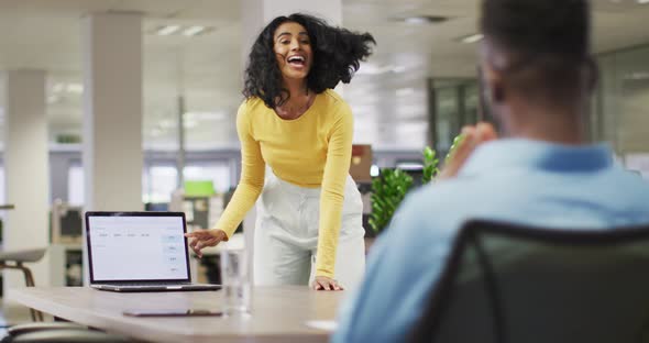 Video of happy biracial businesswoman using laptop and talking with male colleague