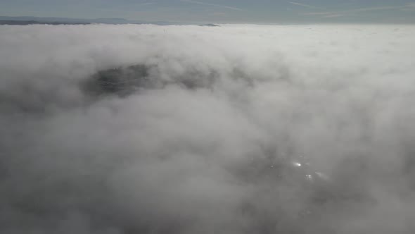 Drone footage above the clouds, showing expanse of white soft fluffy clouds, with mountains in the d