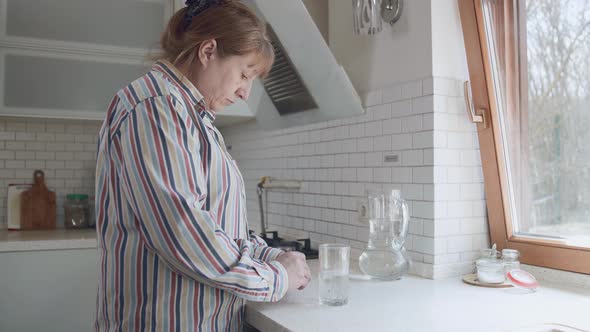 Senior caucasian woman taking pills in the morning in the kitchen