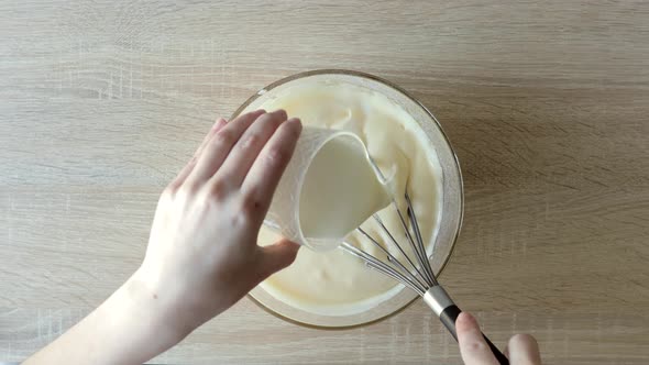 Female hands beating egg whites cream with mixer in the bowl on wooden table.
