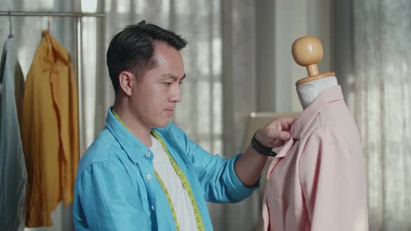 Close Up Of Asian Male Designer With Sewing Machine Wearing Jacket On A Mannequin