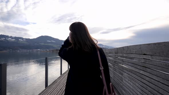 Following shot of a young asian woman doing her hair while walking on a wooden pier in slow motion i