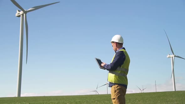 Maintenance Standing Near Wind Mill and Using Tablet