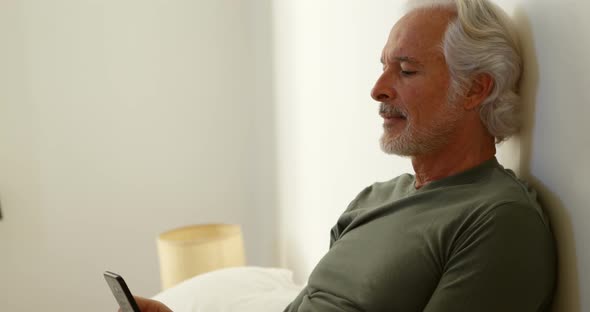 Senior man using mobile phone in bedroom at home 4k