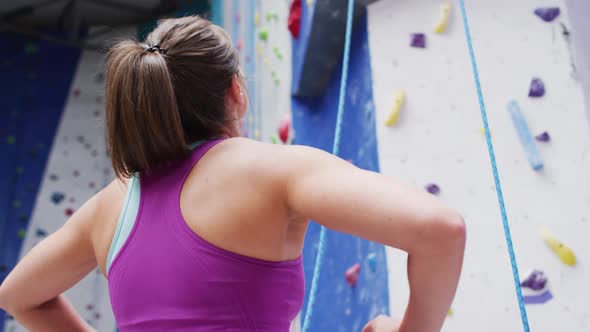 Rear view of caucasian woman preparing to climb a wall at indoor climbing wall