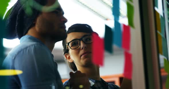 Executives discussing over sticky notes on glass wall