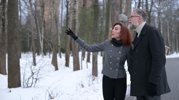 Wife of a gray-haired man shows something in the distance while walking