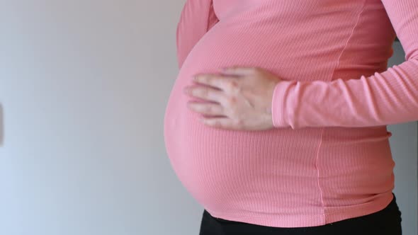 Time for childbirth. Pregnant woman stroking her belly holding a watch in her hands.