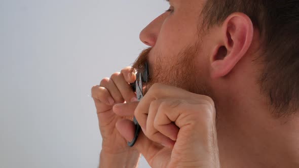 Adult man cutting his own beard and mustache with scissors comb Caucasian red bearded male face 4K