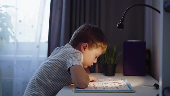 Little boy doing homework at home. kid reading a book at the table by the light of lamp