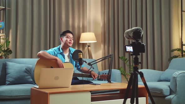 Asian Male With Guitar Talking To Camera, The Man Is Streaming For His Social Media Channel