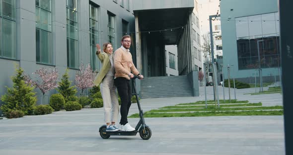 Young Guy and Girl Ride on Electric Scooters Near Business Center at Street Outdoors, After work