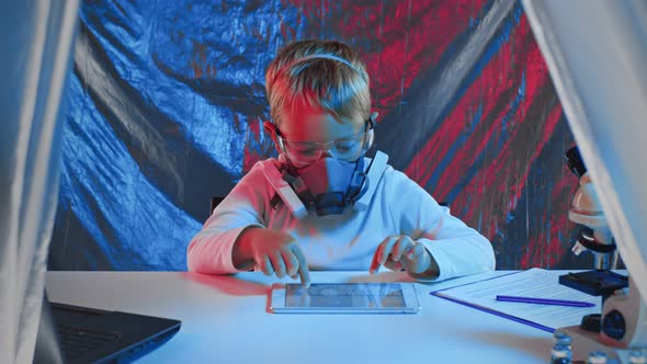 A Little Sientist in Protectiva Mask is Working with Tablet in a Laboratory alt