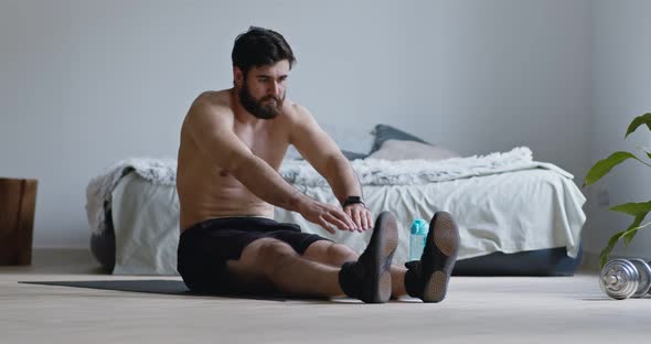 Young Man Doing Stretching Exercise, Sitting on Floor at Home