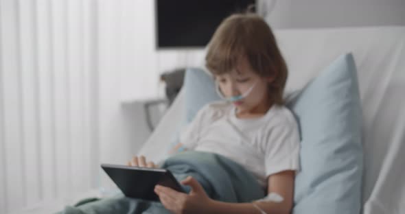 Preteen Kid Patient Lying in Hospital Bed Using Tablet with Dropper in Hand