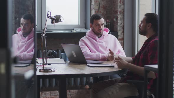 A Young Businessman with a Laptop Talks to a Colleague in the Office