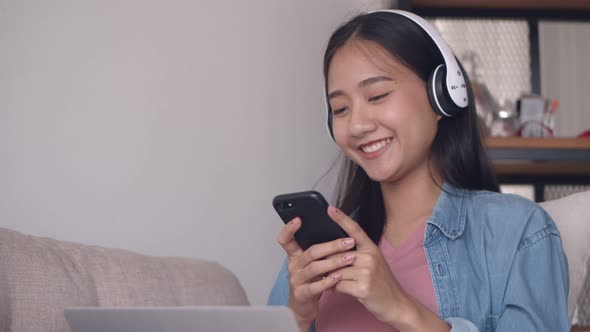 Asian woman listening to music in headphones use smartphone.