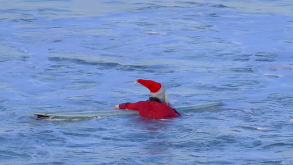 Santa Claus paddles out to go surfing.