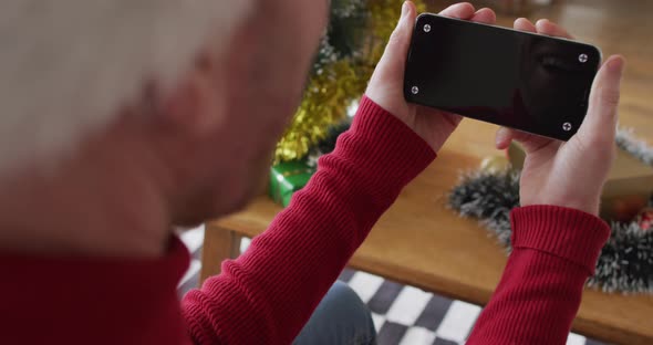 Happy albino african american man wearing santa hat using smartphone at christmas