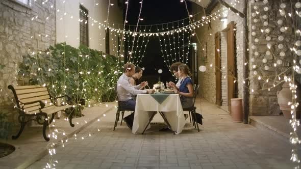 Four People, Two Couples Happy Talking and Eating During a Romantic Gourmet Dinner or Lunch