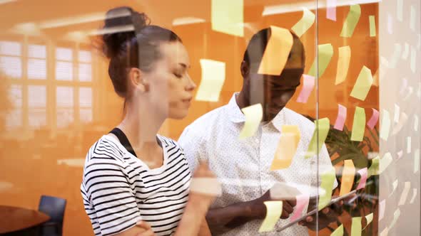 Male and female business executives discussing over digital tablet while reading sticky notes