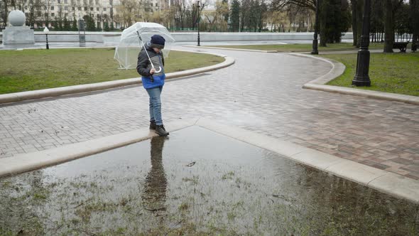 Boy in Jacket Stands Under Umbrella in Park