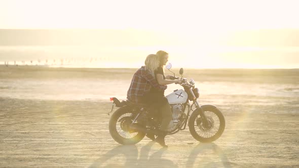 Attractive Young Woman Motorcyclist with His Girlfriend Riding a Motorcycle in a Desert on Sunset or