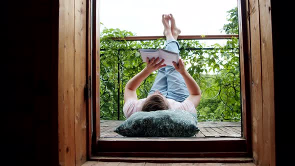 a Man Lies on His Balcony and Reads a Book with His Legs Up