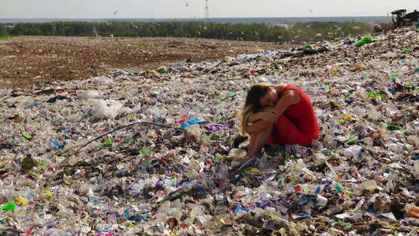 Sad Female Nature Pollution Activist Sits at Huge Trash Dump