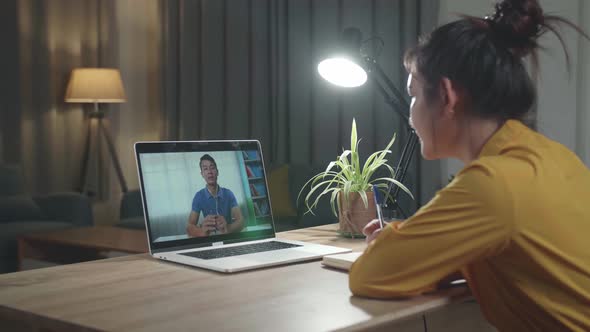 Young Asia Girl Using Laptop Talk To Colleagues About Plan In Video Call Meeting At Living Room