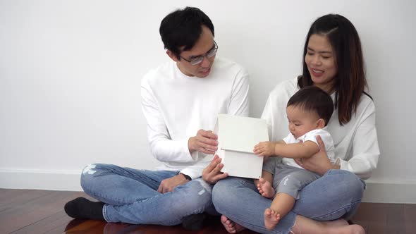 Cheerful Parents Smiling and Showing Toy House to Cute Baby While Sitting on Floor at Home