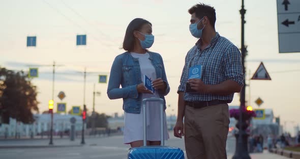 Multiethnic Couple in Safety Mask Standing Outdoors with Luggage and Vaccine Certificate
