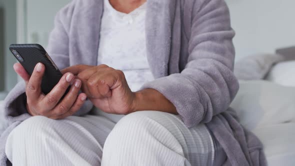 Mid section of african american senior woman using smartphone while sitting on the bed at home