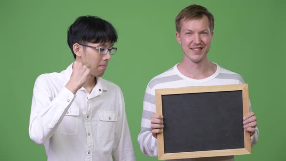 Two Happy Young Multi-ethnic Businessmen Showing Blackboard and Giving Thumbs Up