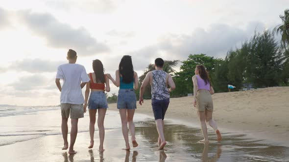Group of Asian young man and woman friends walk on the beach together.